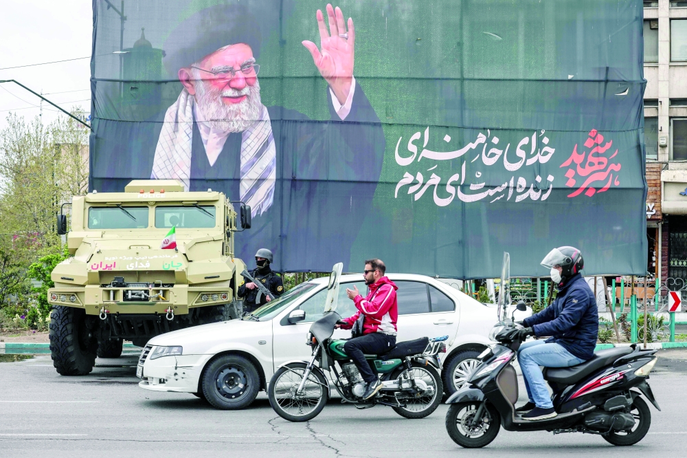 Commuters ride past an Iranian security forces vehcile parked under a banner honouring Iran slain supreme leader Ayatollah Ali Khamenei in Tehran. — AFP