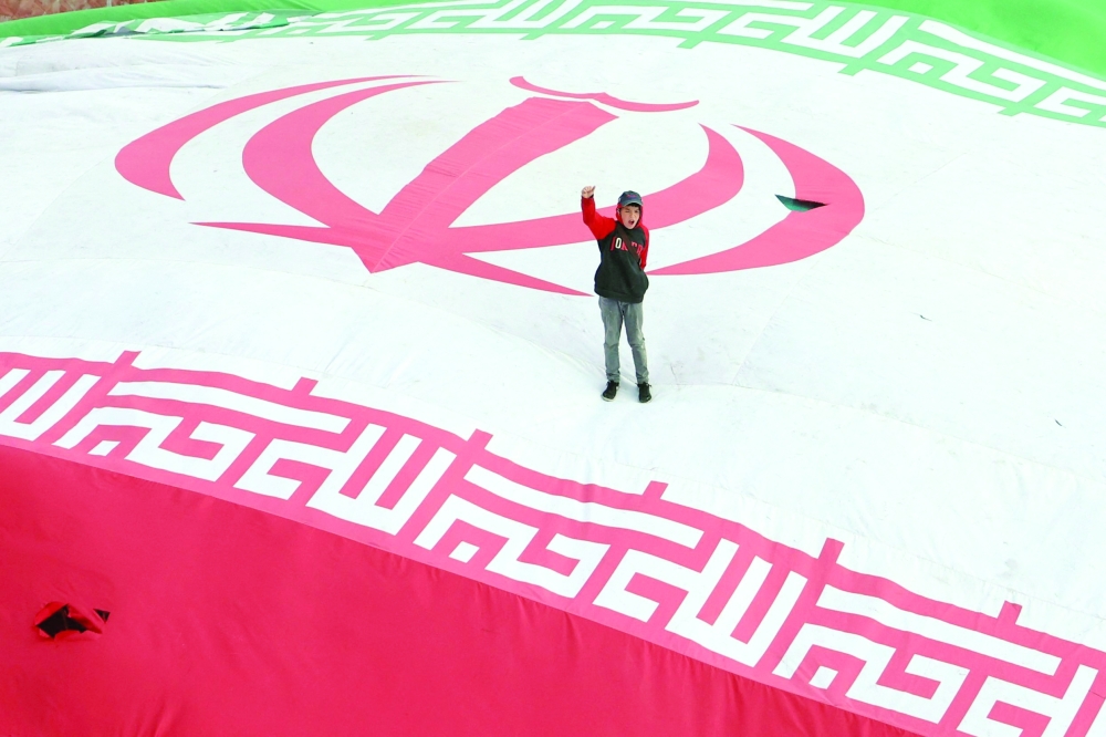 A boy raises his fist while standing on a giant Iranian flag during the funeral of people killed in US-Israeli strikes at Enghelab Square in Tehran. — AFP