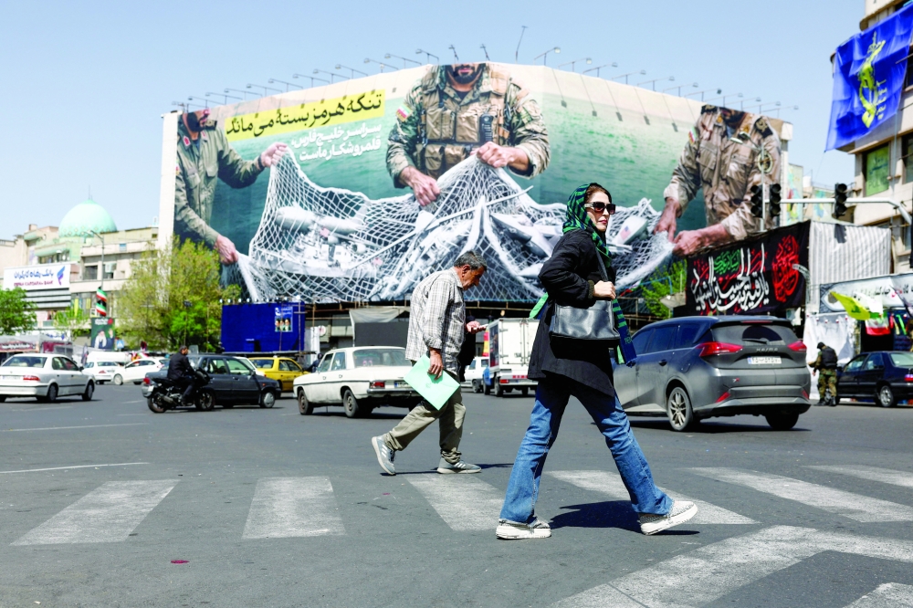 People walk on a street, near an anti-US billboard, in Tehran. — Reuters 