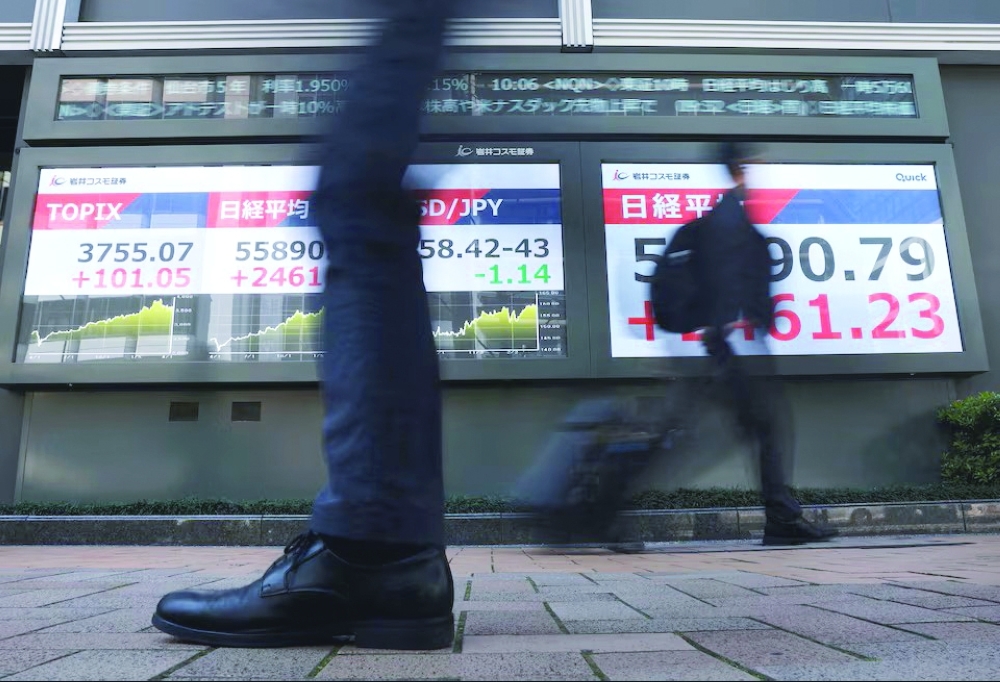 Passersby walk past screens displaying Japan's Nikkei share average, exchange rate between Japanese yen and U.S. dollar and the Tokyo Stock Price Index (TOPIX) outside a brokerage in Tokyo, Japan ــReuters