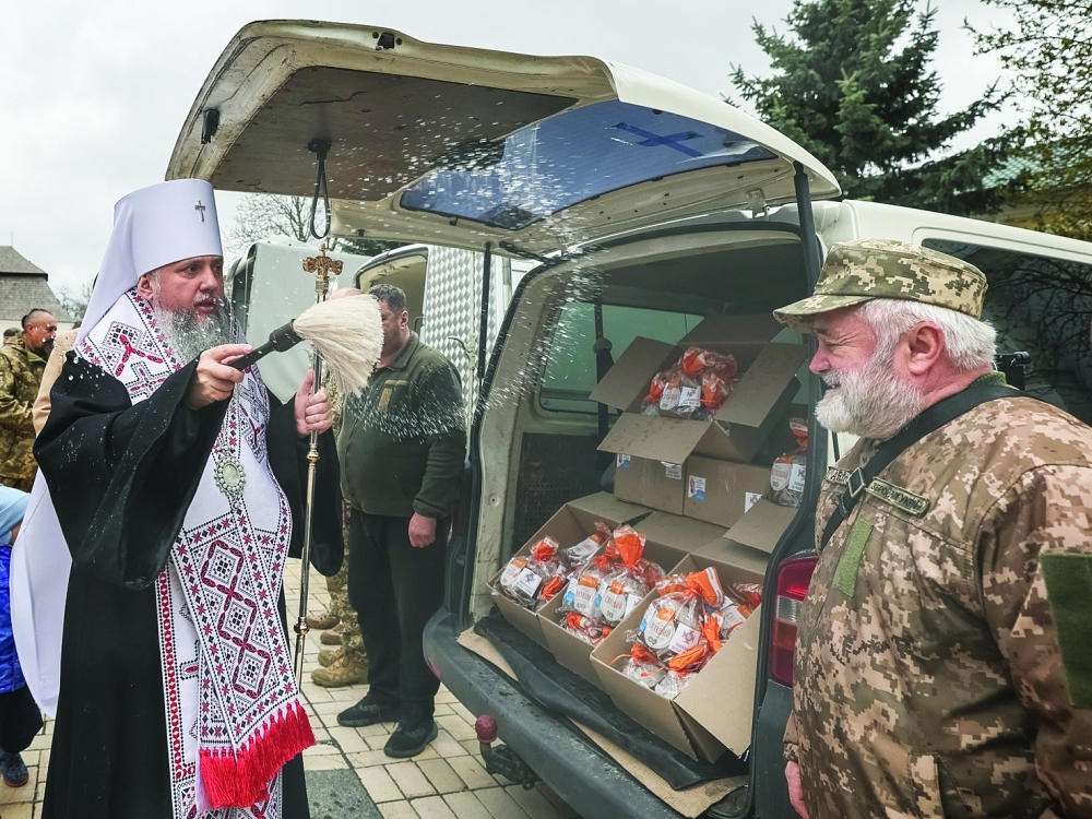 Metropolitan Epiphanius I, head of the Orthodox Church of Ukraine sprinkles holy water on a Ukrainian serviceman next to Easter cakes in Kyiv. — Reuters