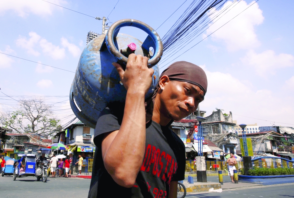 A man carries a tank containing cooking fuel in Mandaluyong, Metro Manila. — Reuters 