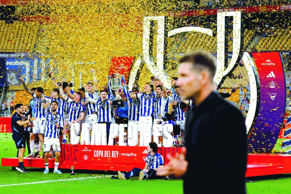 Real Sociedad's Mikel Oyarzabal and teammates celebrate with the trophy after winning the Copa del Rey as Atletico Madrid coach Diego Simeone looks dejected. — Reuters