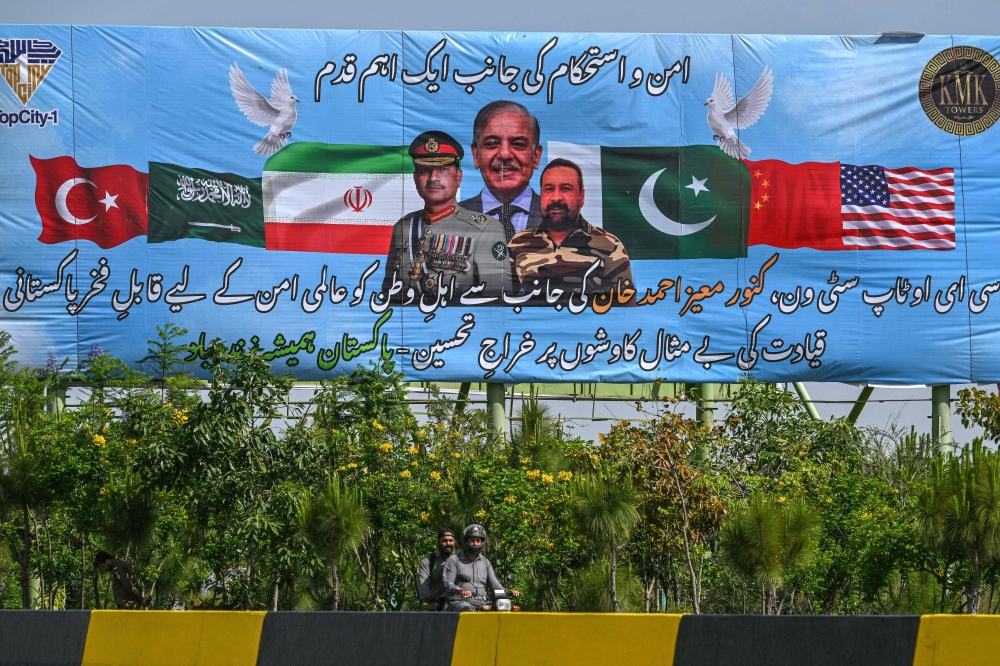 Motorcyclists ride past a billboard featuring Pakistan's Prime Minister Shehbaz Sharif (C) and Army Chief and Field Marshal Syed Asim Munir (L) in Islamabad on April 20, 2026, ahead of anticipated US-Iran peace talks. 