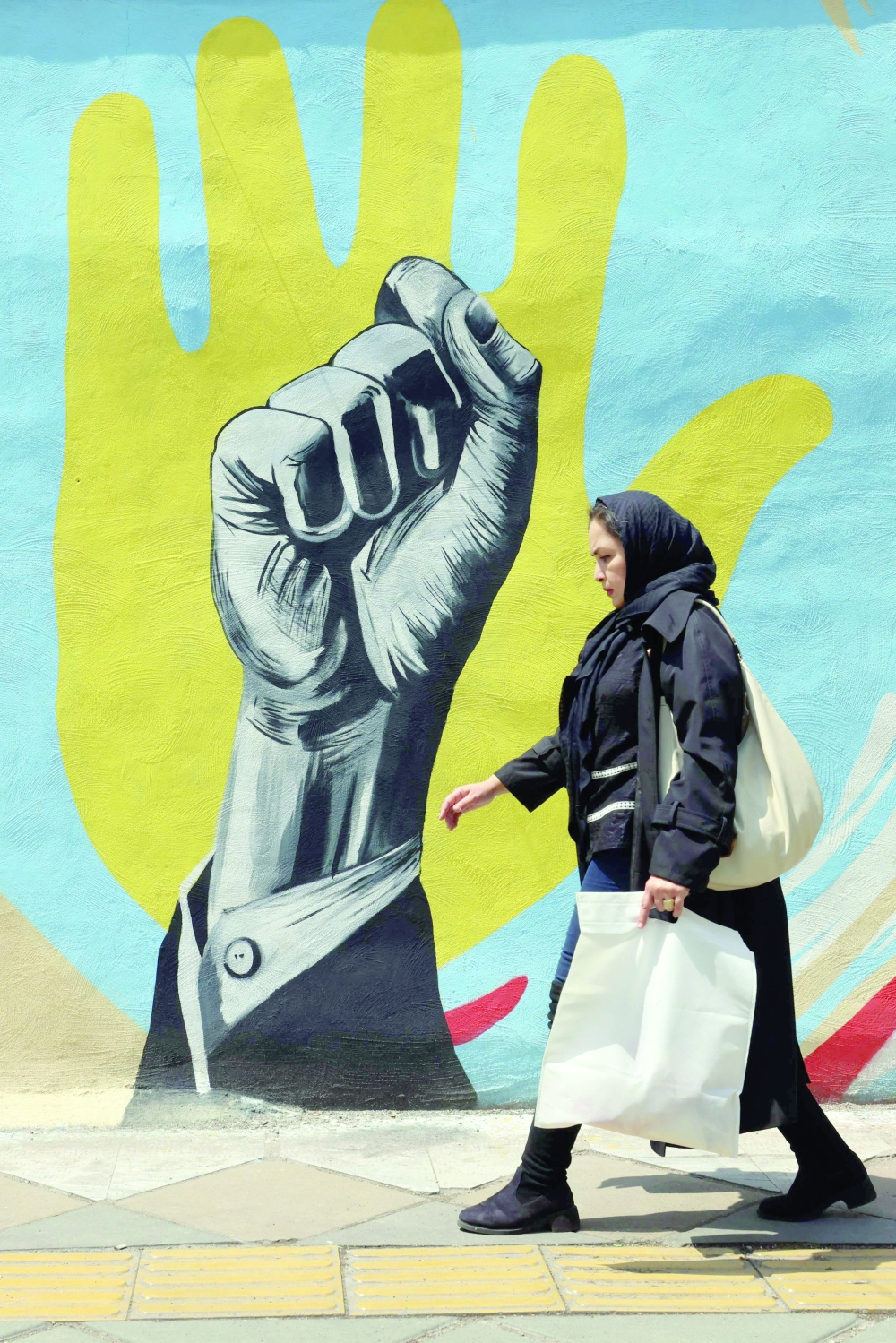 An Iranian woman walks past a mural in Tehran amid a ceasefire in the region, on Tuesday. - AFP