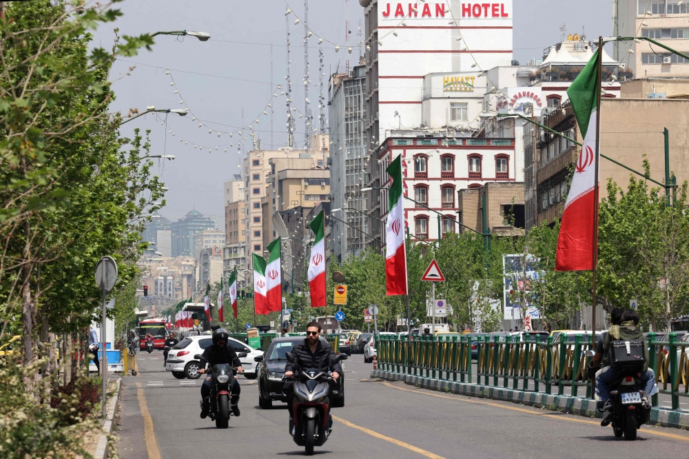 Vehicles and motorbikes drives along a street adorned with the Iranian flag, in Tehran on April 21 2026
