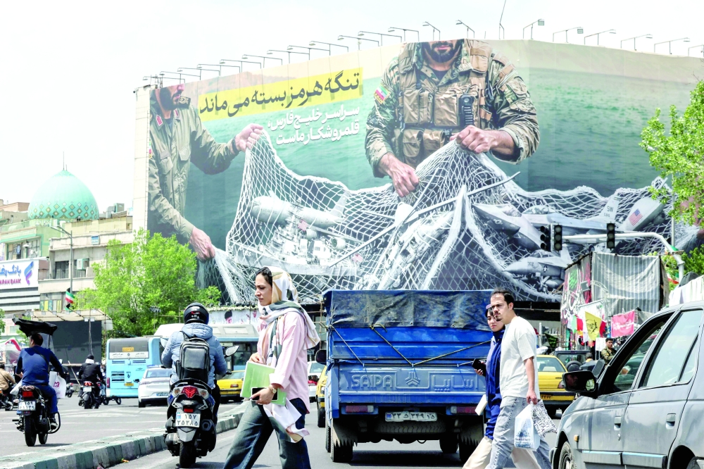 Iranian walks past a giant billboard reading 'The Strait of Hormuz remains closed' at the Revolution Square in Tehran. — AFP