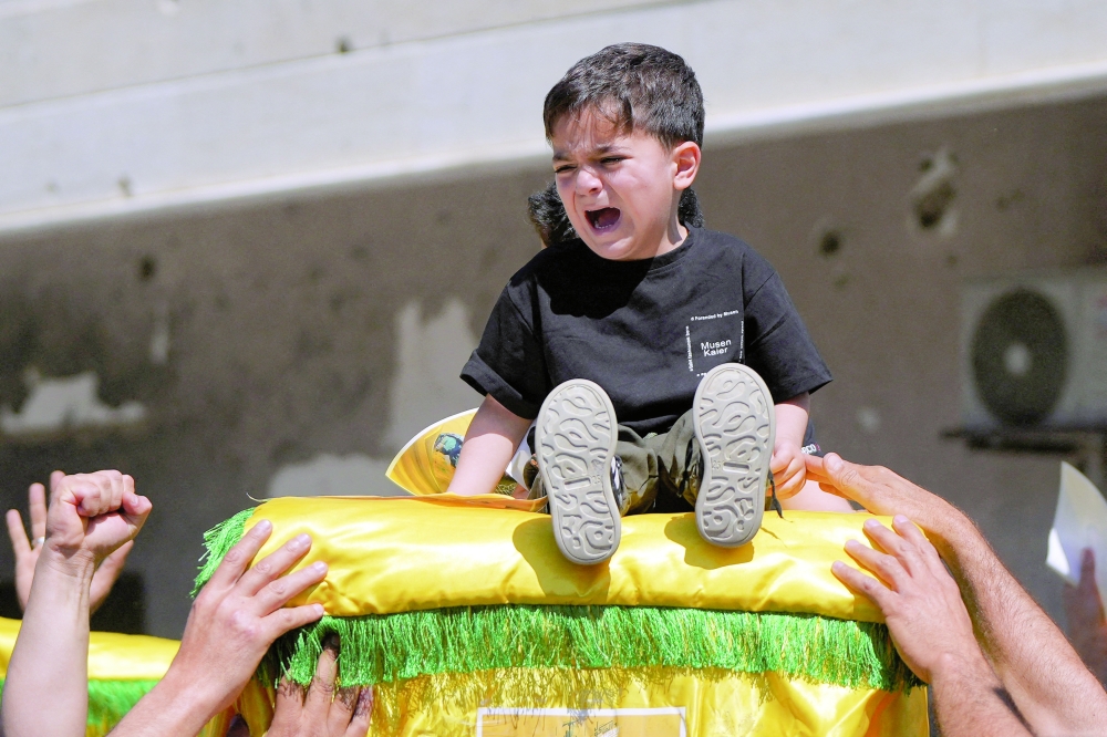 A child cries while sitting on the coffin during a funeral in Mansouri Lebanon, on Thursday. —Reuters