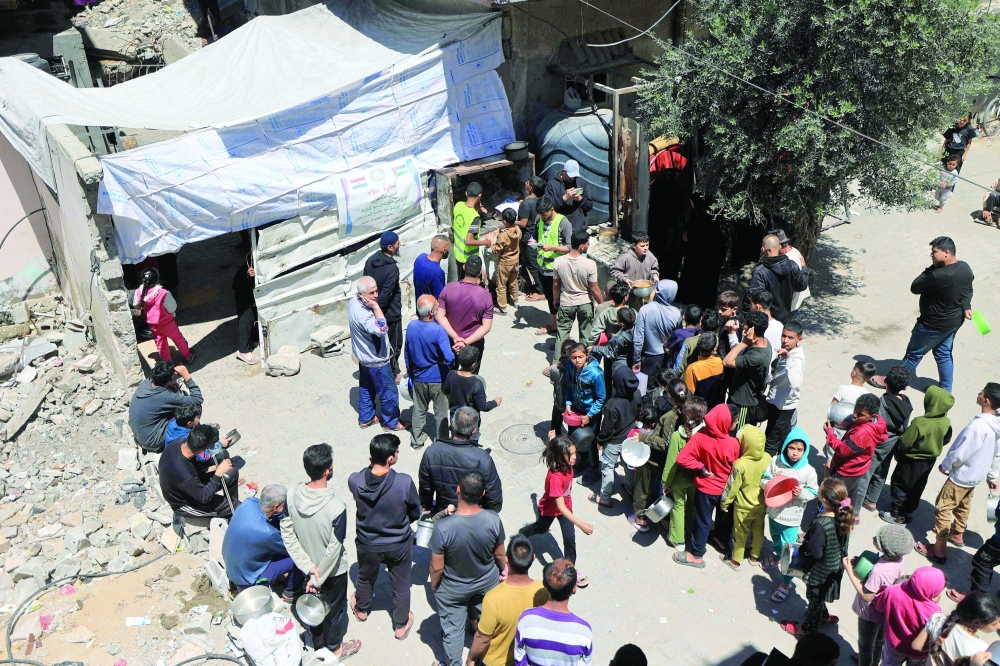 Displaced Palestinians stand near the rubble as they wait to collect food, in the central Gaza Strip. — AFP