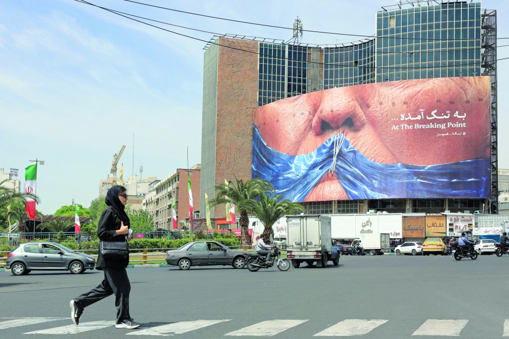 A woman walks past an anti-US billboard referring to President Donald Trump and the Strait of Hormuz, installed on a building at the Valiasr Square in Tehran on Saturday. — AFP