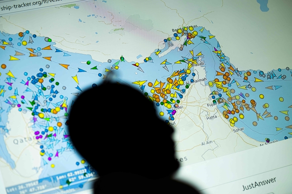 A photo illustration taken in Nicosia on May 4, 2026, shows a person in front of a large screen displaying vessel movements in the Strait of Hormuz on a ship-tracking website