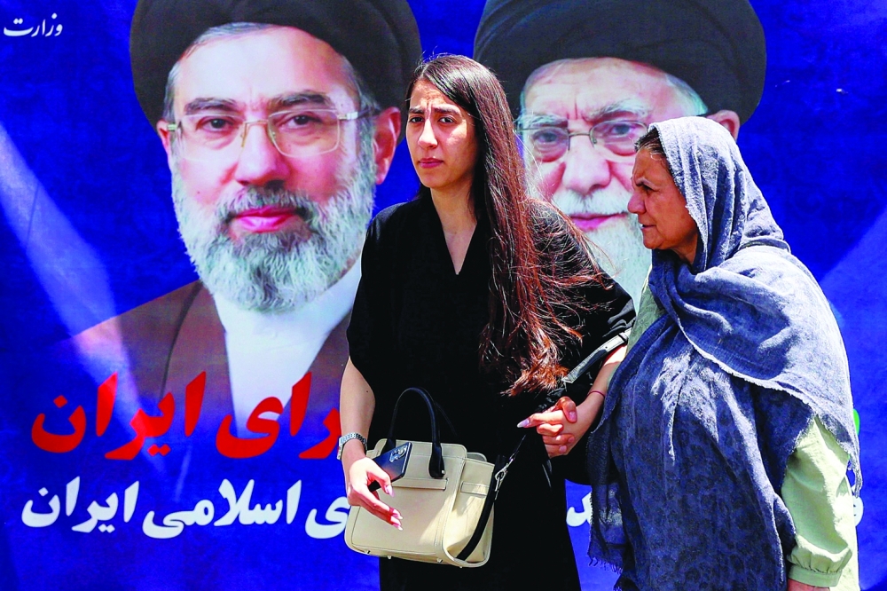 Women walk past a large banner depicting Iran's current supreme leader Ayatollah Mojtaba Khamenei and his predecessor and late father Ali Khamenei along a street in Tehran on Wednesday. - AFP