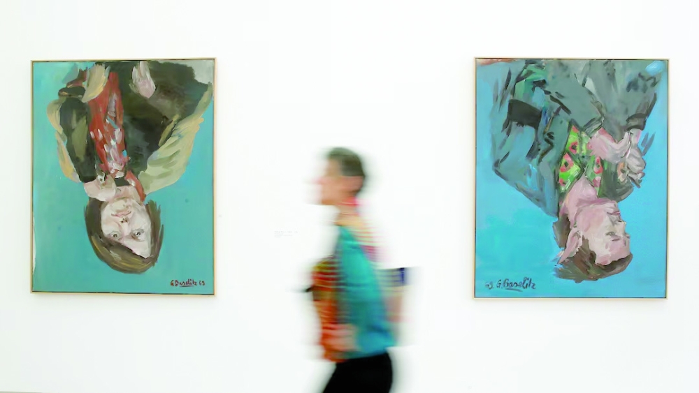 A woman walks past the paintings 'Portrait of Elke I, 1969' and 'Da Portrait (Franz Dahlem), 1969' (R) of German artist Georg Baselitz during a media preview of the exhibition 'Baselitz'. — Reuters