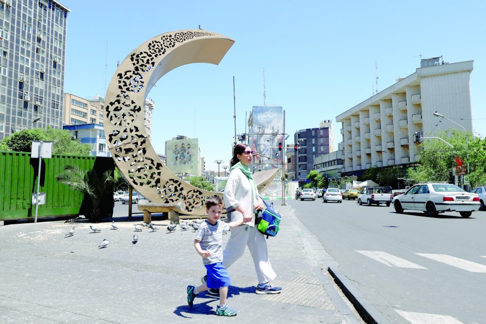 An Iranian woman holds her son's school bag as she leads him towards a busy street in the capital, Tehran, on Saturday. — AFP