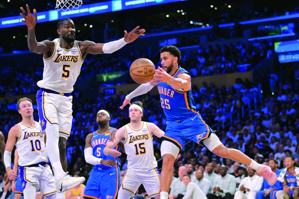 Oklahoma City Thunder guard Ajay Mitchell makes a pass under the basket as he is defended by Los Angeles Lakers center Deandre Ayton. — Imagn Images