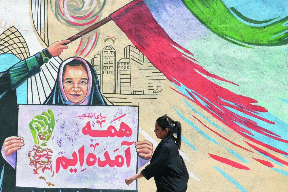 An Iranian woman walks past a mural painted on a wall in the capital Tehran on Sunday. —AFP
