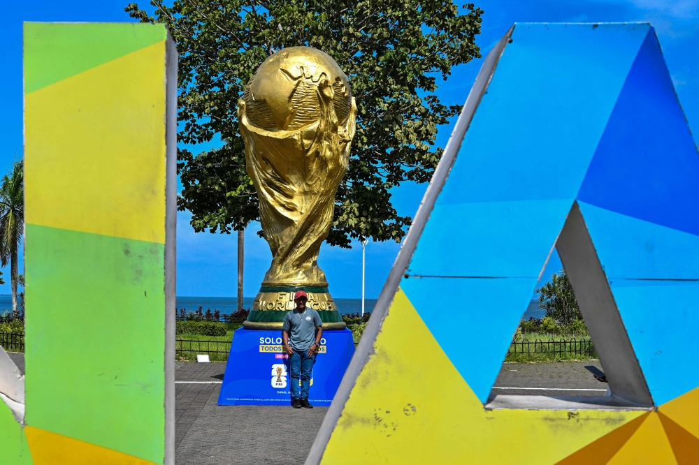 A man poses for a photo in front a giant replica of the FIFA World Cup trophy at the Cinta Costera 