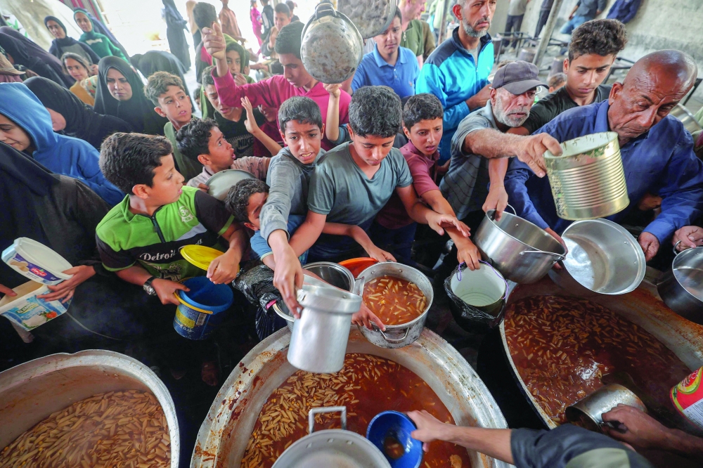 Displaced Palestinians receive food from a charity kitchen at the Nuseirat refugee camp in the central Gaza Strip. — AFP