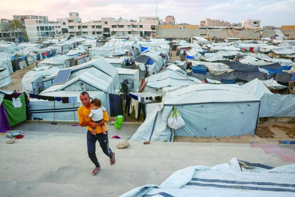 A Palestinian man carries a toddler amid makeshift shelters in Khan Yunis in the southern Gaza Strip. — AFP