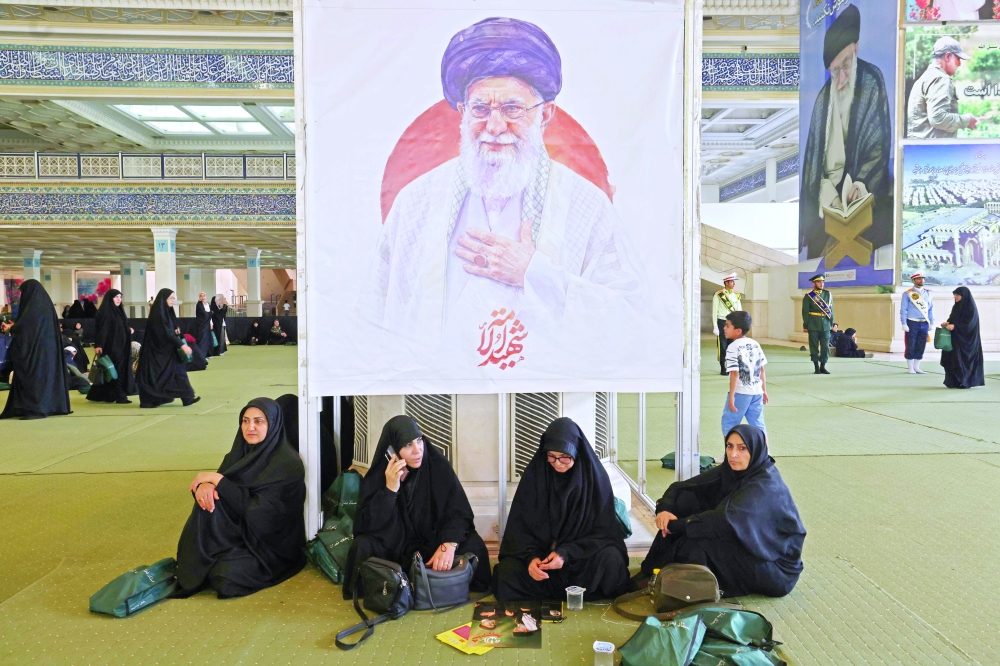 Iranian women sit in front of an image of the late assassinated supreme leader Ali Khamenei, as they gather at Imam Khomeini Mosque in Tehran. — AFP