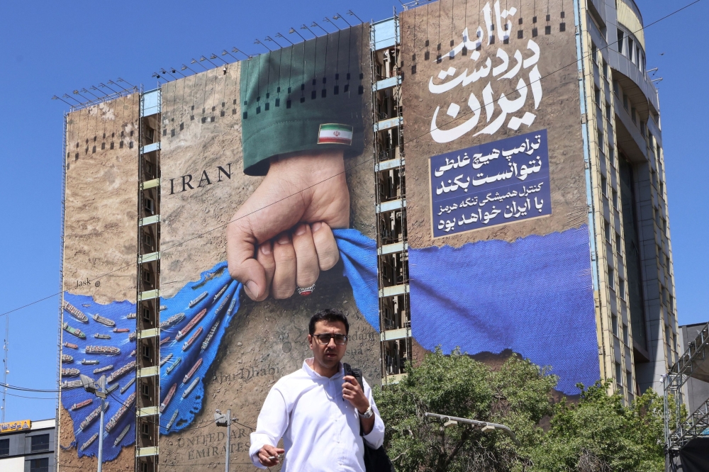  man crosses a street past a billboard on the facade of a building depicting the Strait of Hormuz with a caption in Persian reading "Forever in Iran’s Hand", at Vanak Square in Tehran on May 25, 2026.