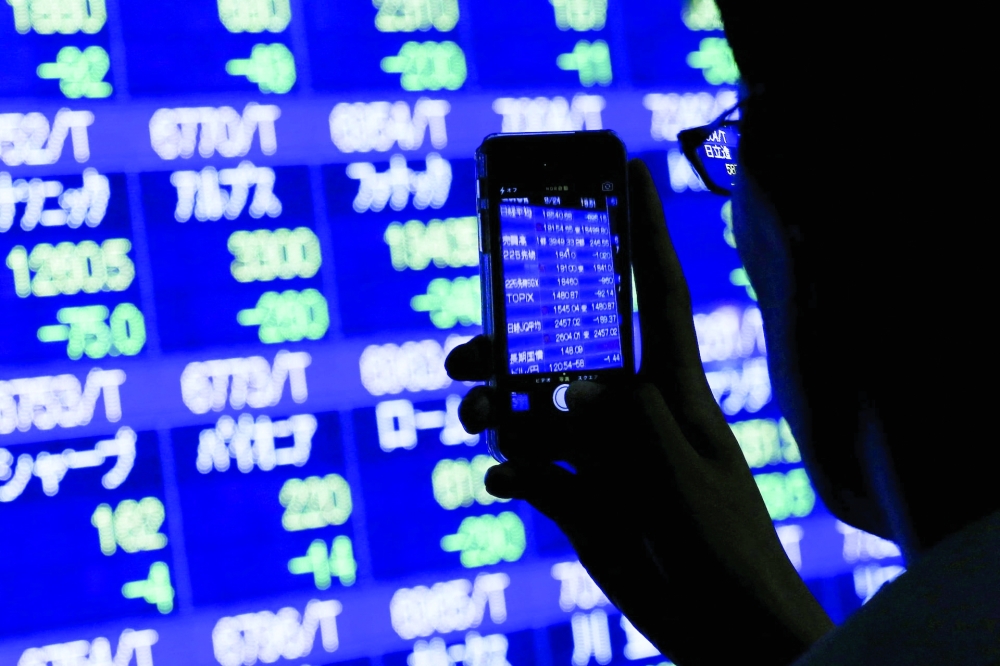 A man uses his phone to take pictures of market indices at a stock quotation board outside a brokerage in Tokyo. — Reuters