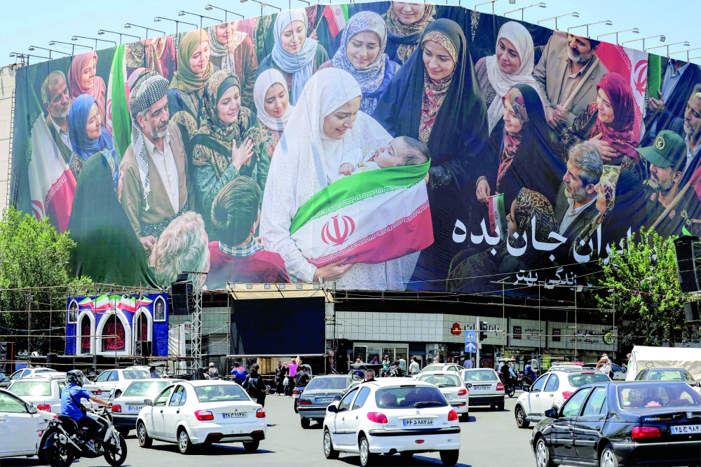Motorists drive their vehicles near a large political billboard along Enghelab Square in central Tehran. — AFP