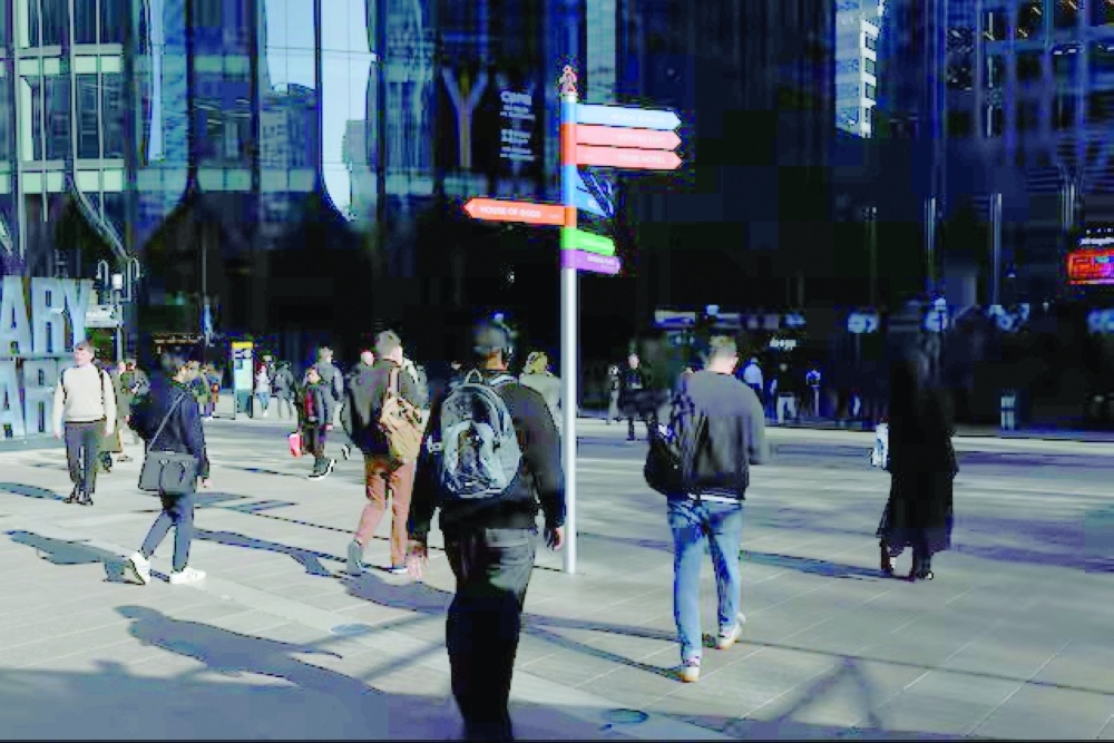People walk past colourful signposts in the financial and business district of Canary Wharf, in London. — Reuters