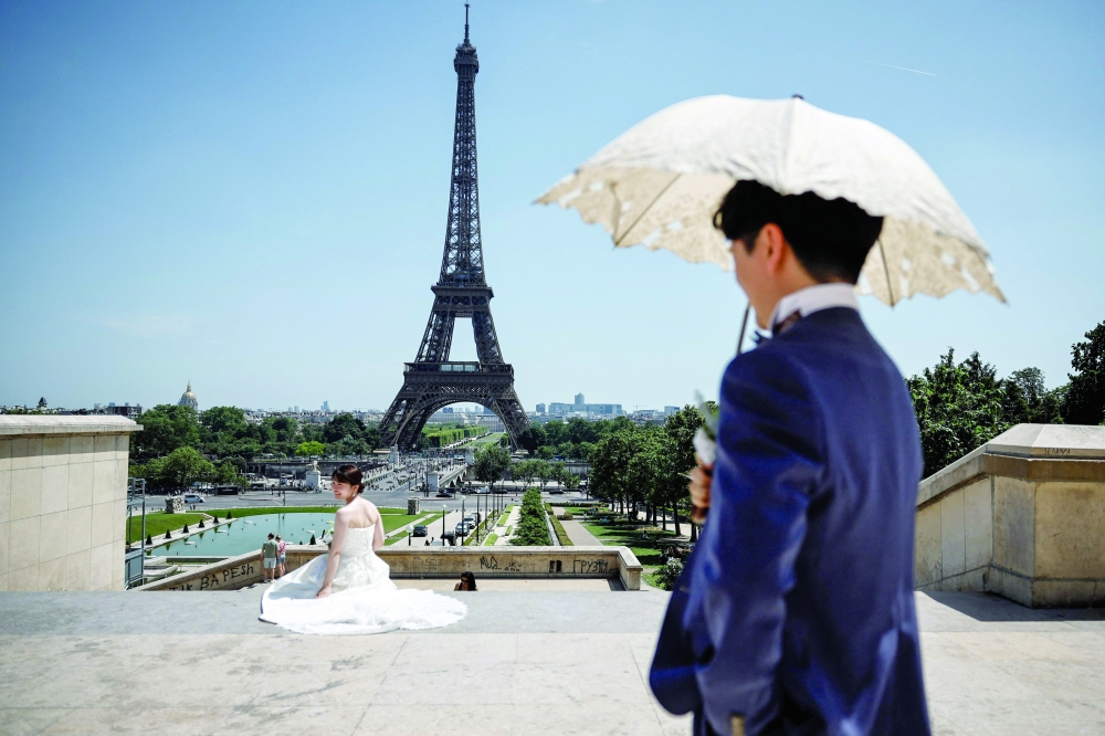 A groom shelters from the sun under an umbrella as a bride sits with a view of the Eiffel Tower in Paris, as a record-breaking early heatwave scorches a swathe of western Europe. - AFP