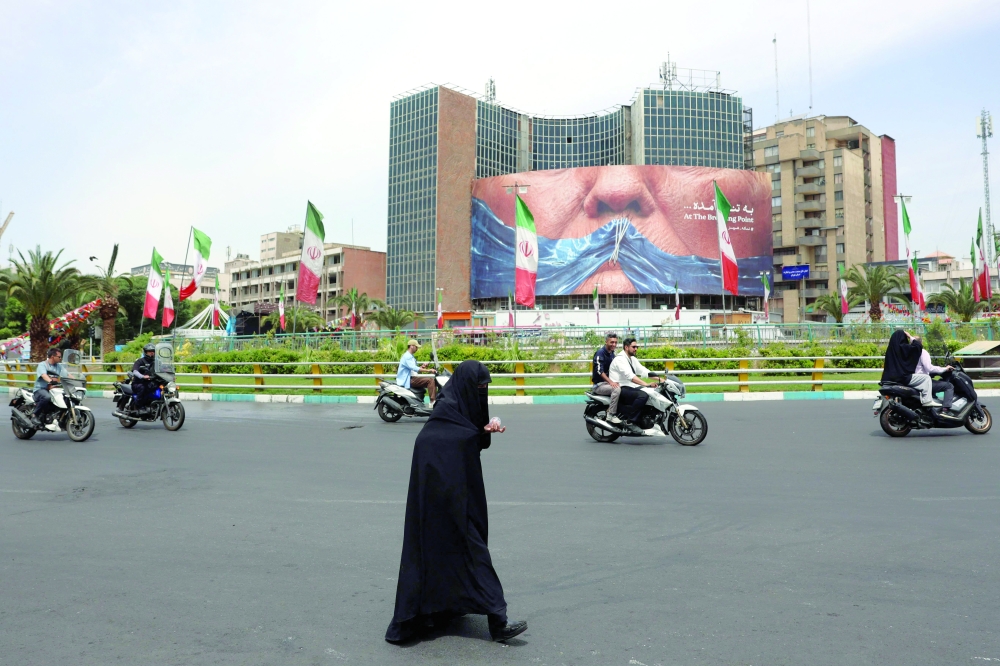 An Iranian woman crosses the road next to a political billboard featuring US President Donald Trump and the Strait of Hormuz erected on a building in Valiasr Square in Tehran. — AFP