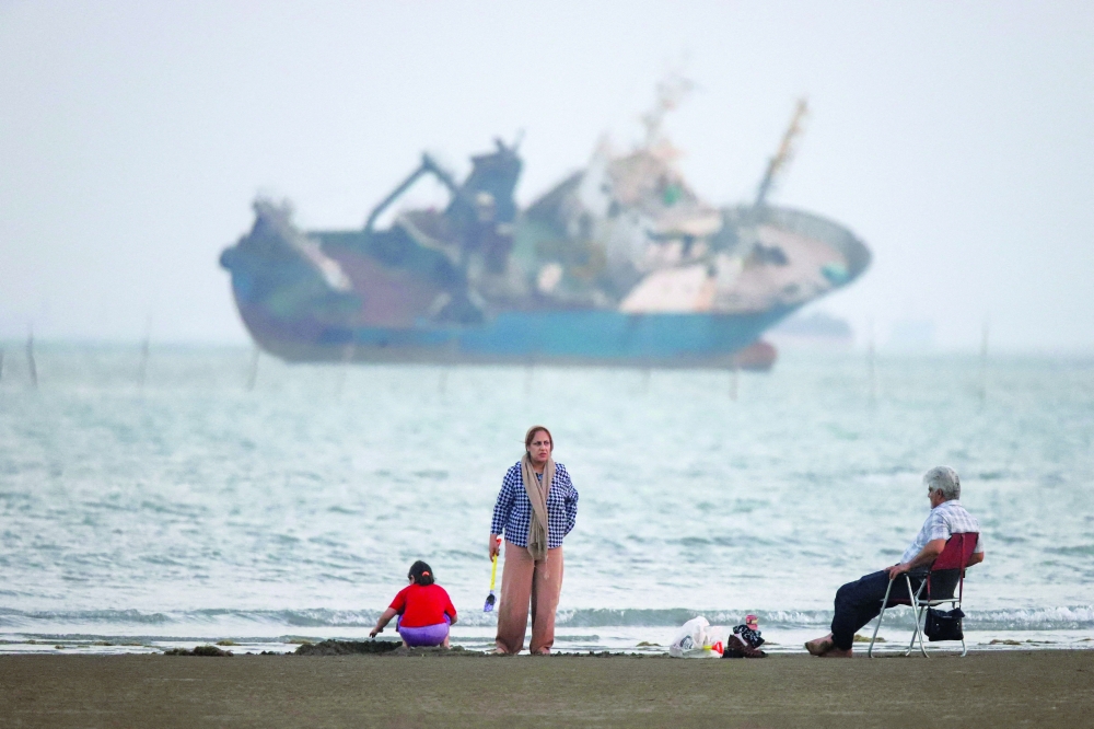 People gather on a beach, as a vessel in the Strait of Hormuz is visible, near the beach of Bandar Abbas, Iran. — Reuters
