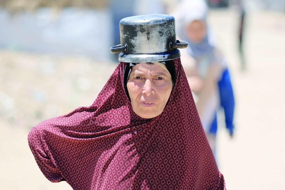 A woman carries a pot on her head as Palestinians gather to receive food from a charity kitchen in Gaza City. — Reuters