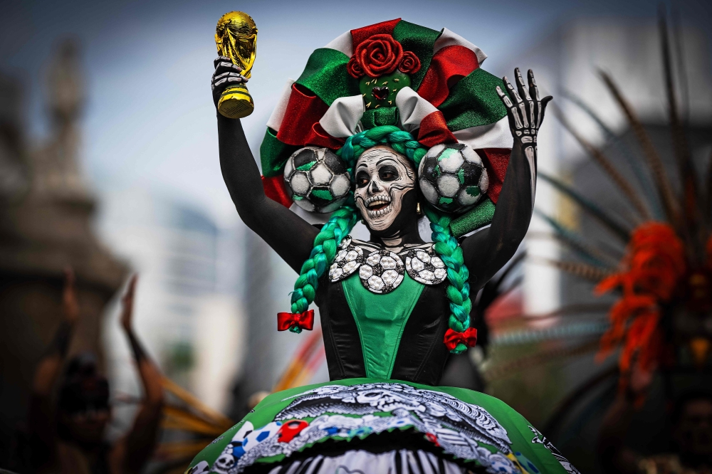 A woman dressed as a Catrina holds up a replica of a World Cup trophy before the start of a Guinness World Record attempt for the world’s largest Mexican Wave 
