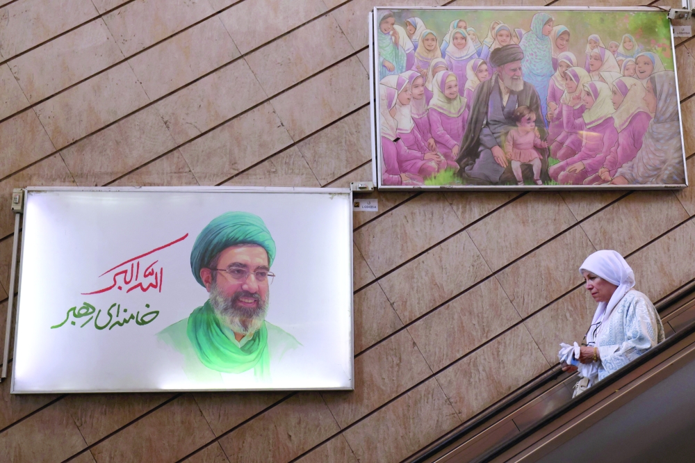 A woman uses an escalator under a photo of Iran’s supreme leader Ayatollah Mojataba Khamenei (L) at a metro station 