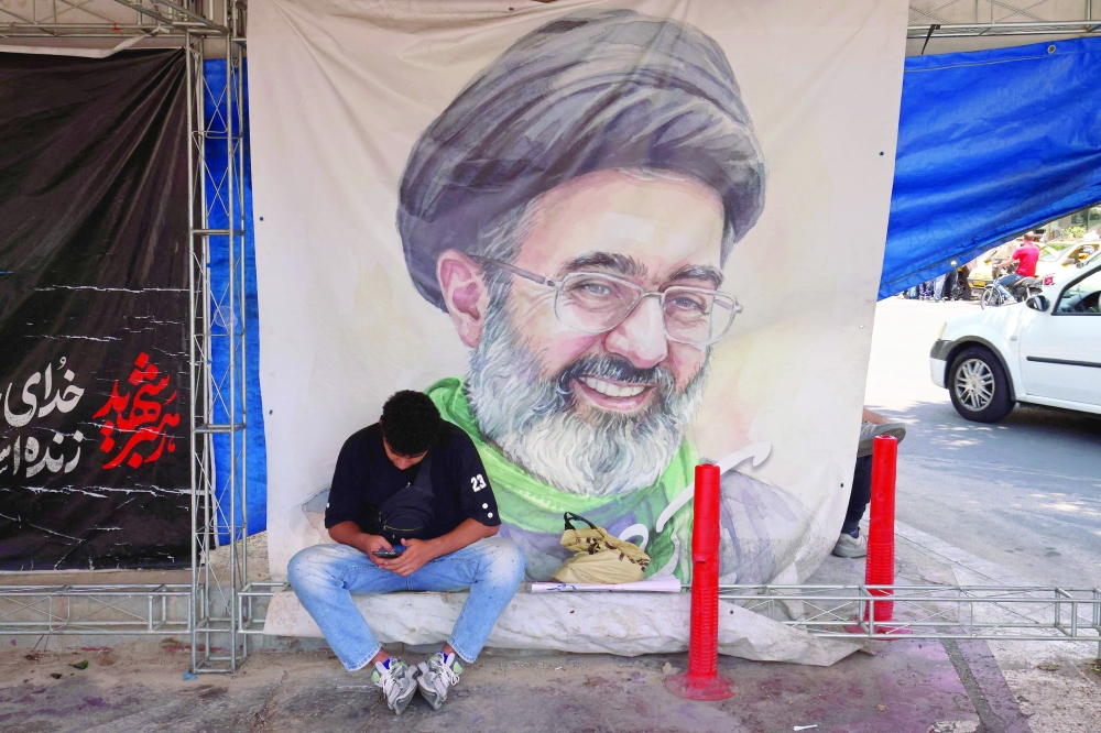 A man sits in front of a poster with a portrait of Iranian Supreme Leader Mojtaba Khamenei, at Vanak Square in Tehran. — AFP 