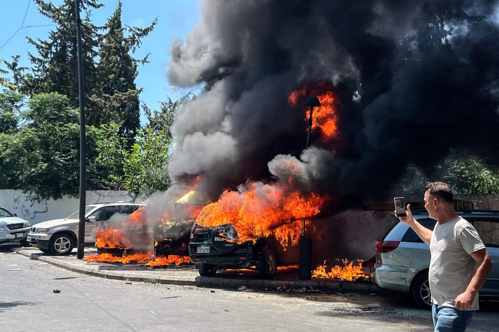 A man takes pictures of burning vehicles following an Israeli airstrike that hit a car in Sidon on June 10, 2026.