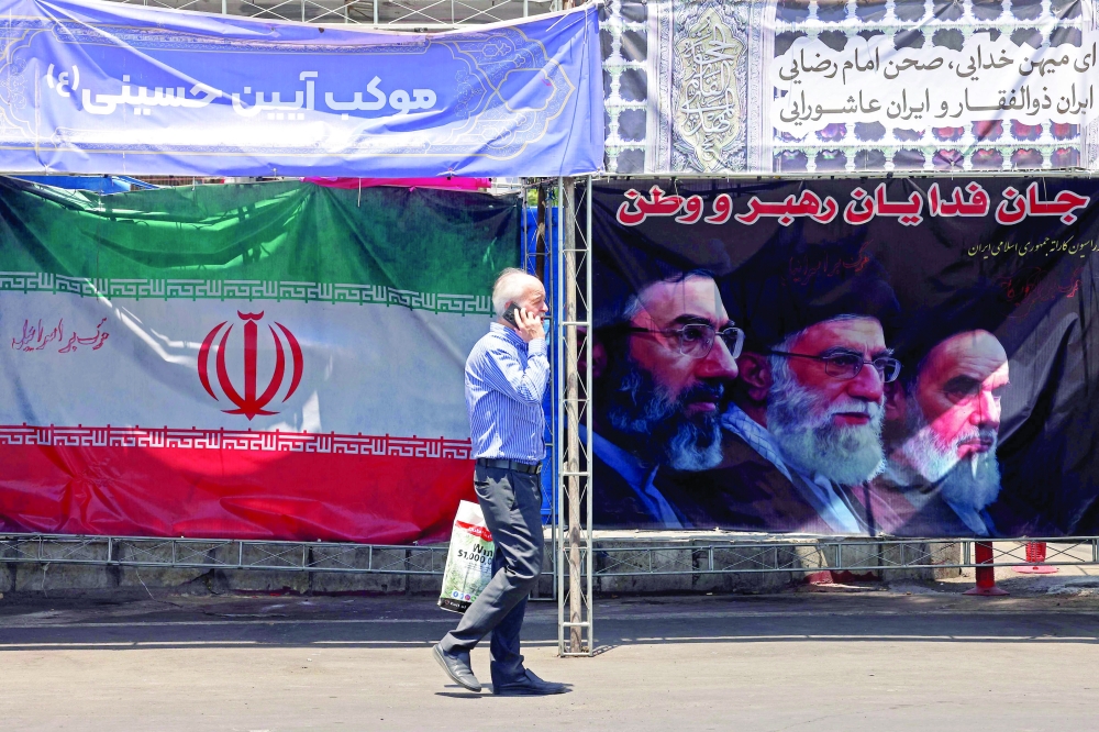 
A man walks past Iran’s national flag and a banner bearing the images of the late founder of the Islamic Revolution supreme leader Ayatollah Ruhollah Khomeini (R), the late Iranian supreme leader Ali Khamenei and his son, the current supreme leader Mojtaba Khamenei (L), erected along a street at the Vanak Square in Tehran. — AFP 