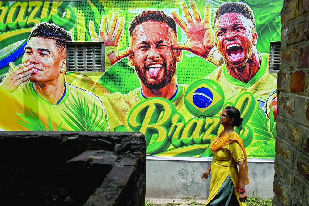 A woman walks past a wall decorated with posters of the Brazil football players on the outskirts of Kolkata