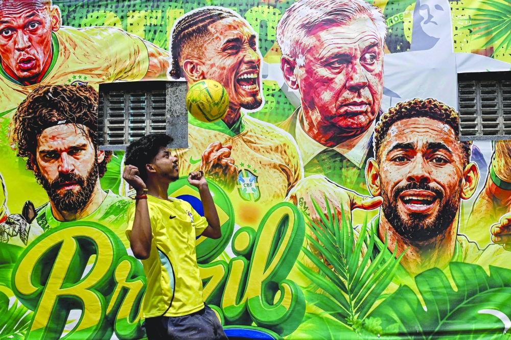 A boy controls a ball next to a wall decorated with posters of the Brazil football squad on the outskirts of Kolkata