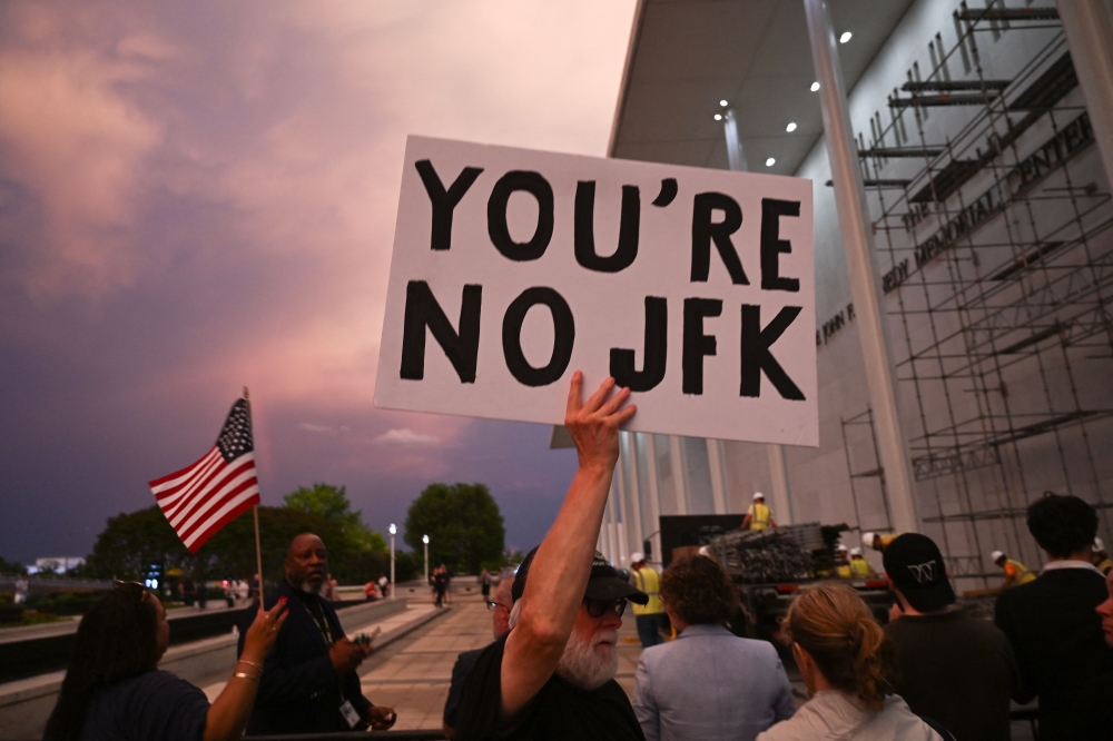  A man holds a sign in protest as people watch as signage is removed on the Donald J. Trump and John F. Kennedy Memorial Center for the Performing Arts in Washington, DC