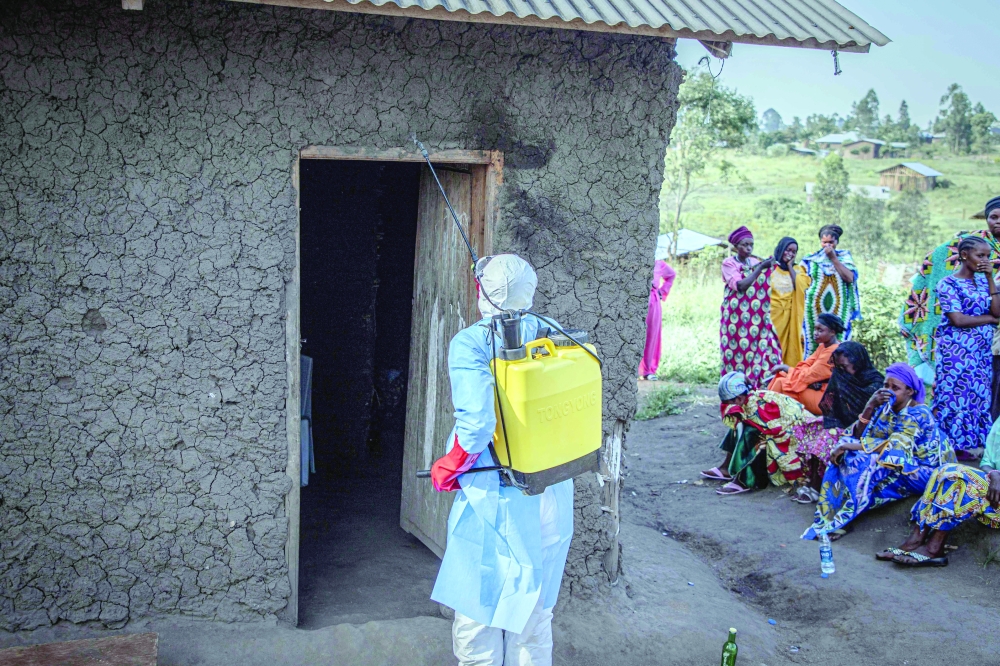 A volunteer, wearing a protective suit, disinfects the door of the house where a child, presumed dead of Ebola virus disease is located, in Bunia. — AFP