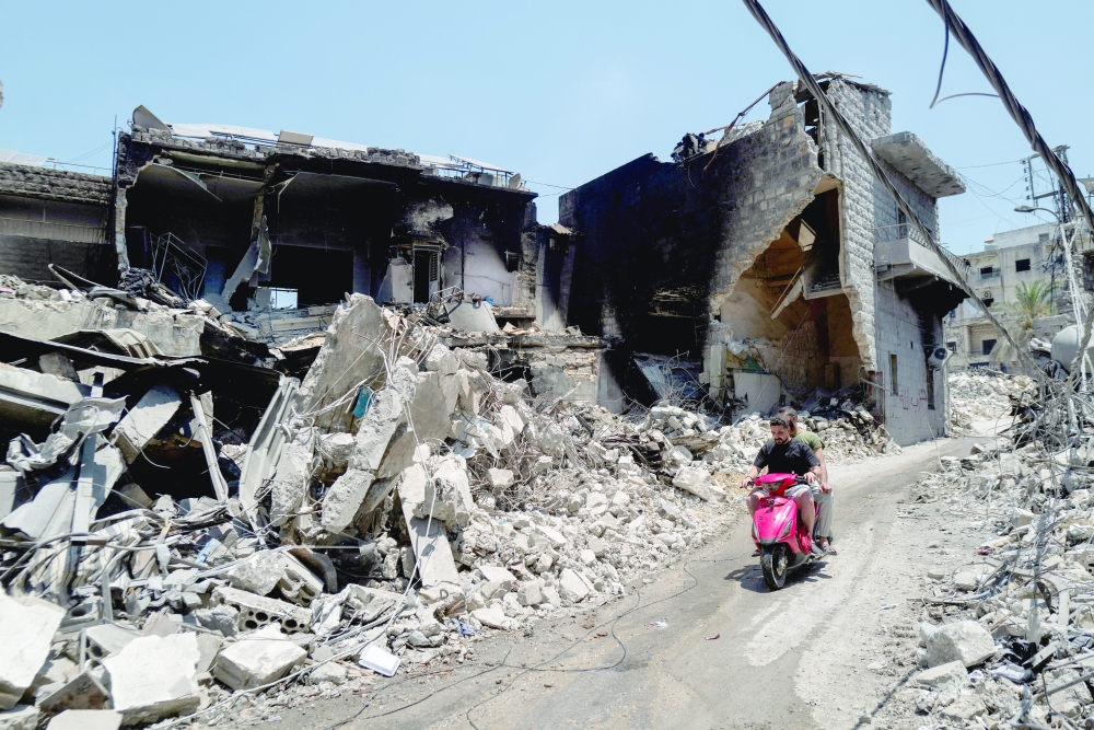 Men ride a motorcycle past shops and buildings damaged by Israeli strikes in Nabatieh, Lebanon, on Wednesday. — Reuters