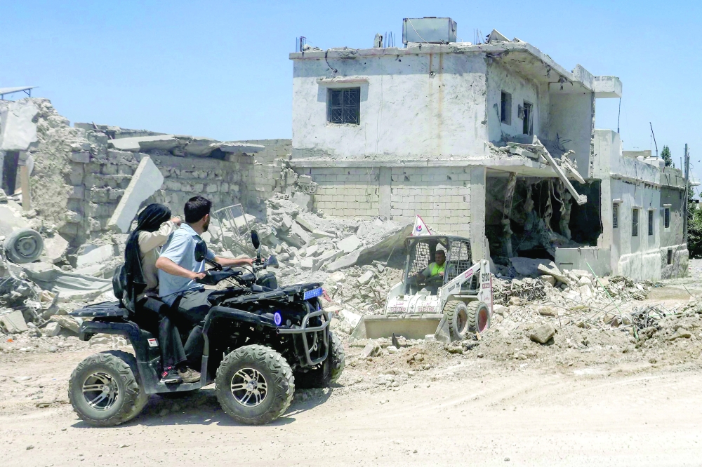 People ride an all-terrain vehicle (ATV) moving past destroyed buildings in the village of Deir Qanoun al-Nahr in southern Lebanon. — AFP