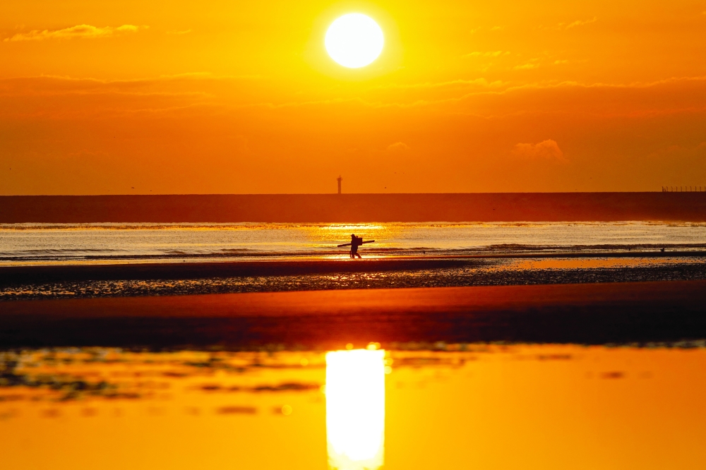 A fisherman walks as the sun rises over the beach of Gravelines, northern France. — AFP