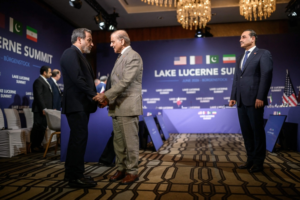 Iran's Foreign Minister Abbas Araghchi (L) shakes hands with Pakistan's Prime Minister Muhammad Shehbaz Sharif (C) next to Pakistan's Chief of Army Staff Field Marshal Asim Munir (R) prior to a quadrilateral meeting between the United States, Iran, Pakistan and Qatar at the Burgenstock luxury hotel complex overlooking Lake Lucerne, Switzerland, on June 21, 2026, as part of high-level talks aimed at advancing a deal to end the Middle East conflict. 