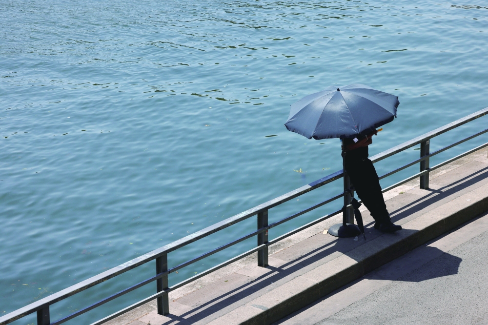 A person shelters from the sun under an umbrella along the banks of the River Seine in Paris. — Reuters 
