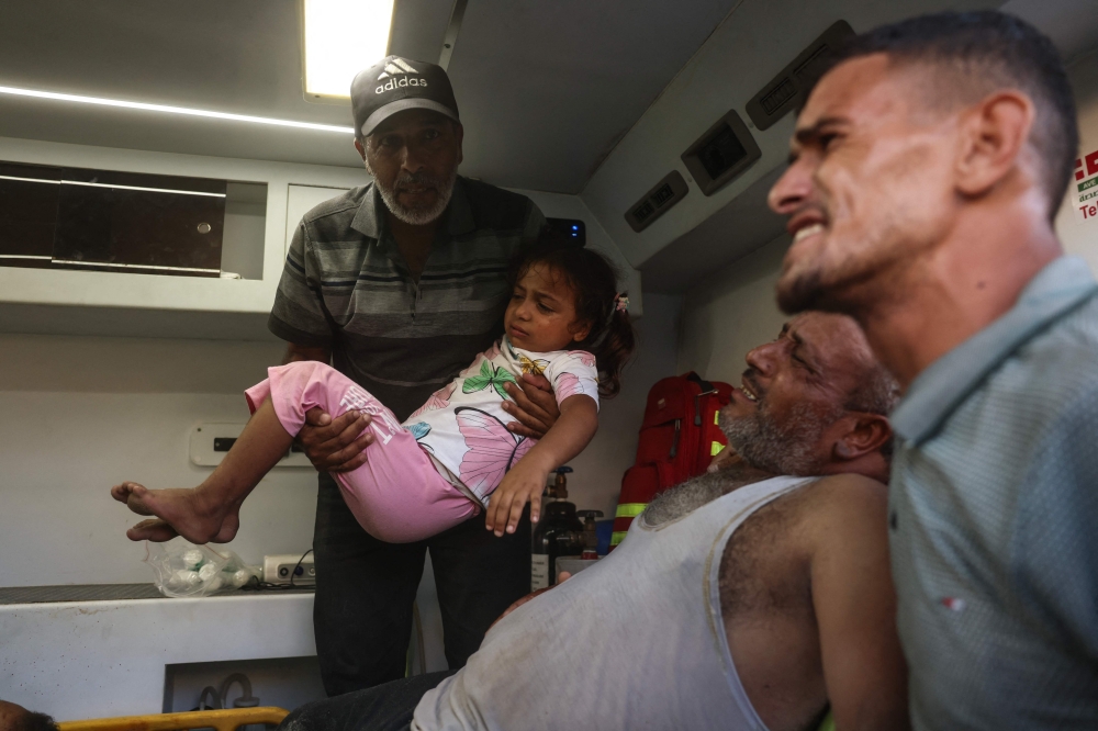 A man carries a girl as casualties arrive by ambulance at Nasser Hospital in Khan Yunis, in the southern Gaza Strip, on June 17