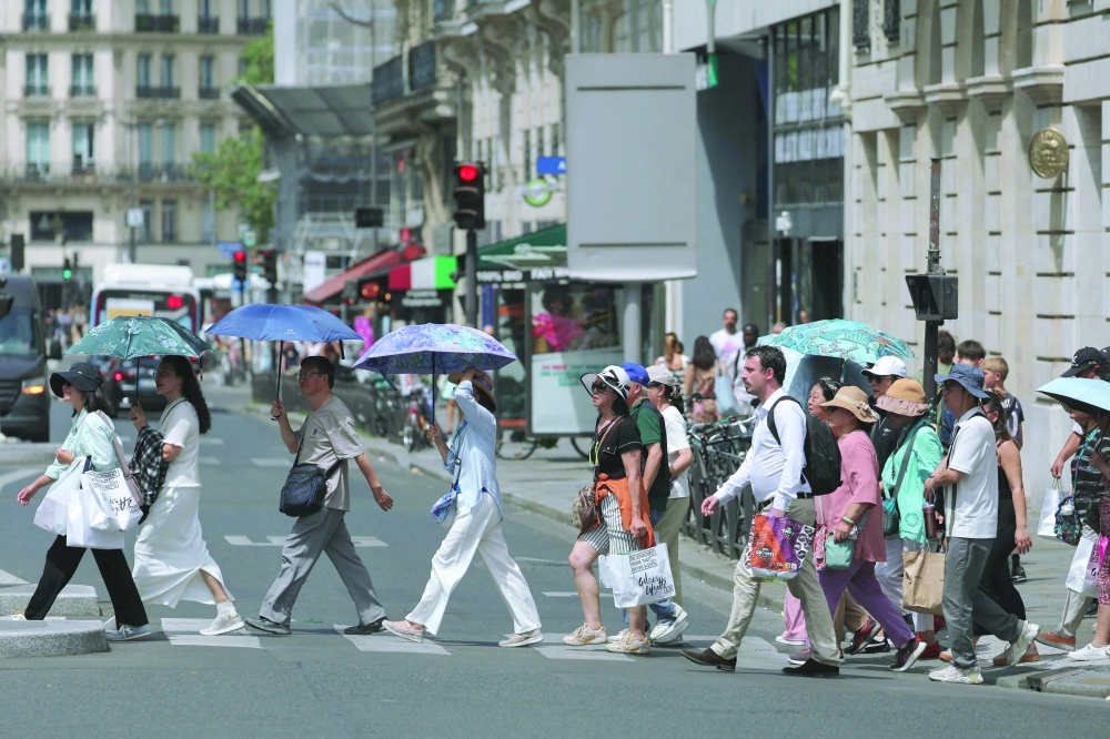 Tourists protect themselves from the sun under umbrellas while crossing a street in Paris. — AFP