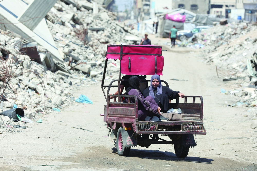 Palestinians ride past the rubble of residential buildings destroyed during the Israeli offensive, in Gaza City. — Reuters 