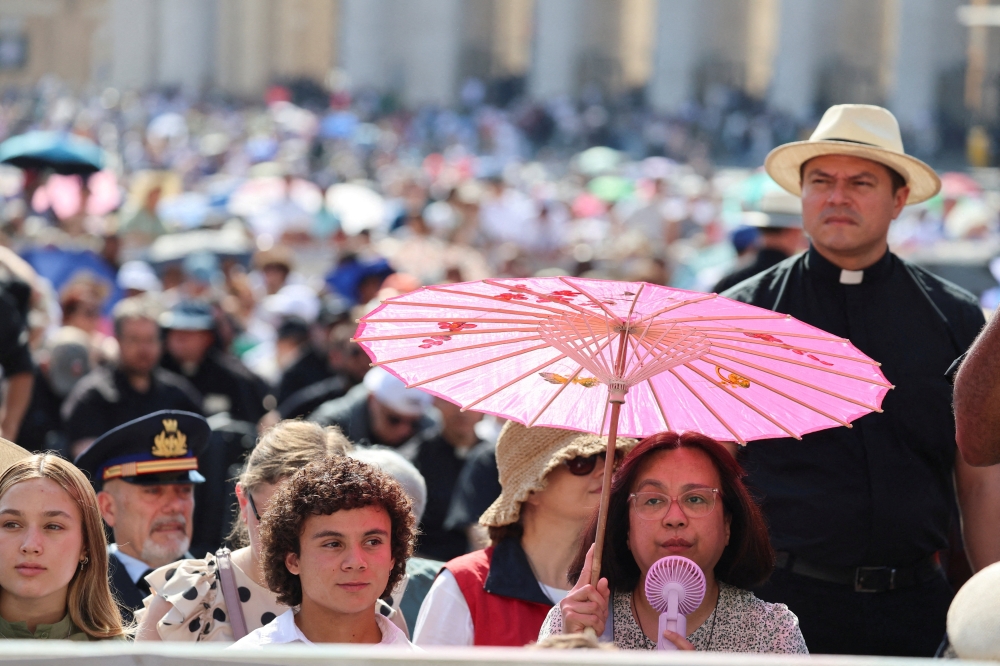 A woman holds a portable electric fan as she shelters herself from the sun under an umbrella on the day Pope Leo holds the weekly general audience in St. Peter's Square at the Vatican
